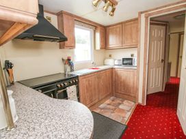 A kitchen with wooden cabinets a black stove a microwave and red carpeted floor at 2 Old Orchard Brockton near Much Wenlock