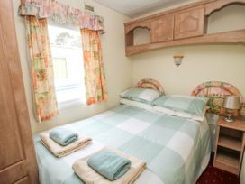 A bedroom with a double bed two folded towels on top a window with patterned curtains and wooden cabinets above the bed at 2 Old Orchard in Brockton near Much Wenlock