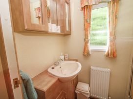 A bathroom sink with wooden cabinets and a window with patterned curtains at 2 Old Orchard Brockton near Much Wenlock