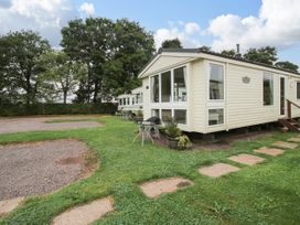 Two beige mobile homes with windows and small outdoor tables on grass with a gravel path and trees at 4 Old Orchard in Brockton near Much Wenlock