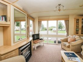 A living room with armchairs a TV on a table a fireplace and large windows at 4 Old Orchard in Brockton near Much Wenlock