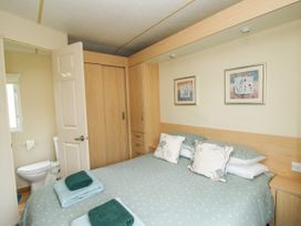 A bedroom with a bed, pillows, towels on the bed, wooden wardrobe, and an open door leading to a bathroom at 4 Old Orchard in Brockton near Much Wenlock