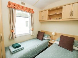A bedroom with two single beds a window with curtains and overhead wooden cabinets at 4 Old Orchard in Brockton near Much Wenlock