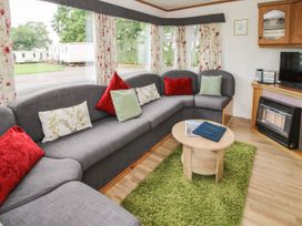 A living room with a gray L-shaped sofa with pillows a round wooden coffee table on a green rug and a fireplace with a TV at 5 Old Orchard in Brockton near Much Wenlock