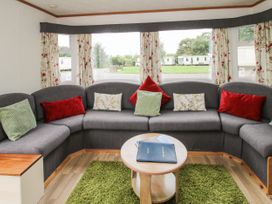 A sitting area with a gray corner sofa with cushions a round wooden table and green rug at 5 Old Orchard Brockton near Much Wenlock