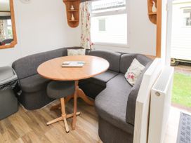 A dining area with a round wooden table surrounded by gray upholstered seating and floral cushions at 5 Old Orchard in Brockton near Much Wenlock