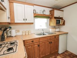 A kitchen with wooden cabinets white upper cupboards a sink under a window a gas stove a microwave a kettle and a mini fridge at 5 Old Orchard in Brockton near Much Wenlock