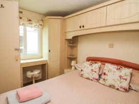 A bedroom with a bed with floral pillows a desk and stool under a window and built in wooden cupboards at 5 Old Orchard in Brockton near Much Wenlock