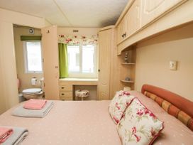 A bedroom with a bed with floral pillows a vanity desk with stool and an adjacent bathroom at 5 Old Orchard in Brockton near Much Wenlock