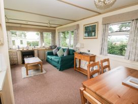 A living room with a green sofa, wooden coffee table, desk with lamp, wooden dining table and chairs at 7 Old Orchard in Brockton near Much Wenlock