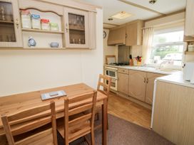 A kitchen with wooden cabinets a wooden dining table with chairs glass jars on a wall cabinet and a window showing an outdoor area at 7 Old Orchard in Brockton near Much Wenlock