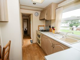 A kitchen with wooden cabinets a gas stove a sink a window with a curtain and a chair at 7 Old Orchard Brockton near Much Wenlock