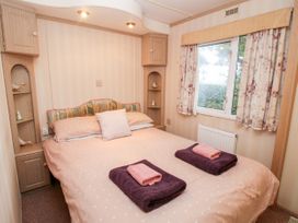 A bedroom with a double bed with towels on it and a window with floral curtains at 7 Old Orchard Brockton near Much Wenlock