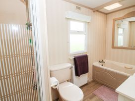 A bathroom with a toilet, bathtub, shower with striped glass door, window, towel on radiator, and mirror at 7 Old Orchard in Brockton near Much Wenlock