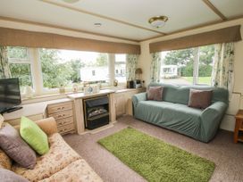 A living room with two sofas a green rug a fireplace and windows at 8 Old Orchard in Brockton near Much Wenlock