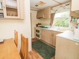 A kitchen with wooden cabinets a gas stove a green rug and a window with floral curtains at 8 Old Orchard Brockton near Much Wenlock