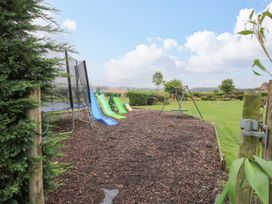 A playground area with slides a trampoline a swing set and grassy field at 8 Old Orchard in Brockton near Much Wenlock