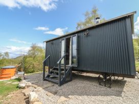 A small black corrugated metal cabin on wheels with stairs leading to open double doors and a wooden hot tub outside at Coraldie in Laggan near Newtonmore