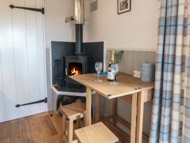 A small wooden dining table with two glasses and a bottle next to a stove with fire in a room with plaid curtains at Coraldie Laggan near Newtonmore