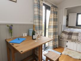 A small wooden table with a blue folder a pen a champagne bottle and two glasses next to plaid curtains and a bed at Coraldie in Laggan near Newtonmore
