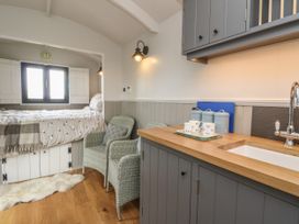 A small kitchen area with grey cabinets a wooden countertop a sink and two wicker chairs next to a bed with white bedding at Coraldie in Laggan near Newtonmore
