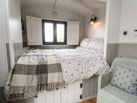 A small bedroom with a bed under a window a wall lamp and a wicker chair with a cushion at Coraldie in Laggan near Newtonmore