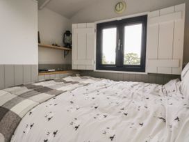 A bedroom with a bed covered in sheep patterned bedding near a window with white shutters and shelves with books and a lantern at Coraldie in Laggan near Newtonmore