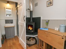 A room with a wood stove burning next to a small wooden table with a vase of flowers and a blue biscuit tin at Coraldie Laggan near Newtonmore