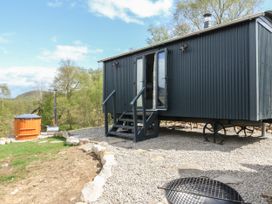 A small black corrugated metal cabin on wheels in a gravel yard with steps and an outdoor wooden hot tub at Coraldie Laggan near Newtonmore