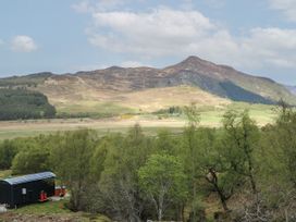 A landscape with trees a small building at the bottom left and hills in the background at Coraldie Laggan near Newtonmore