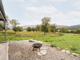 A gravel patio with a fire pit and trees on grassy land at Coraldie in Laggan near Newtonmore