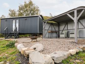 An outdoor area with a small dark grey cabin on wheels next to a covered seating area with two chairs and a table at Coraldie in Laggan near Newtonmore