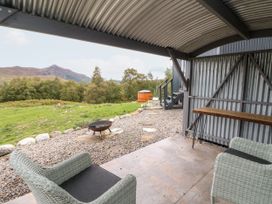 A covered outdoor seating area with two chairs a fire pit and wooden table overlooking a grassy landscape with trees and hills at Coraldie in Laggan near Newtonmore