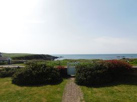 A view of the sea and a gate surrounded by bushes at Faraway in Rhosneigr