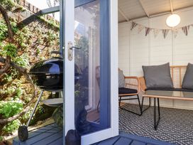 A seating area with wicker furniture and cushions next to an open door leading to a patio with a black barbecue grill at Kestrel Cottage Southwold
