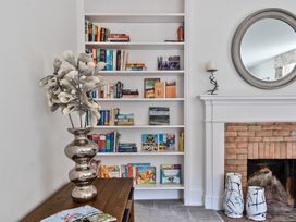 A bookshelf with books and a wooden table with a metallic vase next to a fireplace with blue and white ceramic vases and a round mirror on the wall at Bedingfield House nr Debenham Debenham
