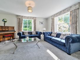 A living room with two blue sofas a glass coffee table a wooden piano and floral curtains at Bedingfield House nr Debenham