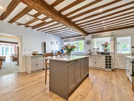 A kitchen with wooden beams on the ceiling an island with chairs and flowers on it and white cabinets at Bedingfield House nr Debenham Debenham
