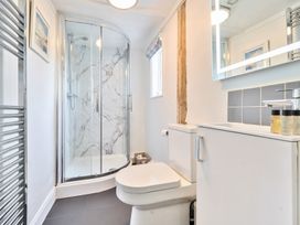 A bathroom with a corner shower, toilet, sink cabinet, towel radiator, and a small window at Bedingfield House, nr Debenham in Debenham