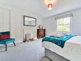 A bedroom with a bed covered with a teal blanket and rolled towels near window a wooden chest of drawers a teal chair and a white fireplace at Bedingfield House nr Debenham Debenham