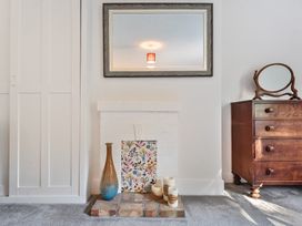 A room with a white painted fireplace decorated with a vase candles and a floral panel and a wooden dresser with a round mirror at Bedingfield House nr Debenham Debenham