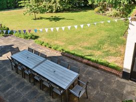 An outdoor patio with a long rectangular table and chairs on a paved area overlooking a lawn with a tree and bunting at Bedingfield House nr Debenham Debenham