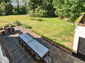 An outdoor patio with a long table and chairs near a brick barbecue and a lawn with trees in the background at Bedingfield House nr Debenham Debenham