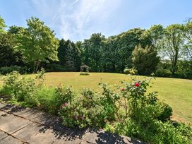 A garden with a stone patio and flower bushes overlooking a lawn and trees at Bedingfield House nr Debenham Debenham