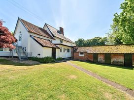 A white house with a tiled roof and an adjoining brick building with green doors in a grassy yard at Bedingfield House nr Debenham Debenham