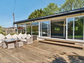 An outdoor wooden deck with wicker furniture and glass table beside large sliding glass doors at Bedingfield House nr Debenham Debenham