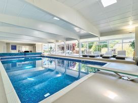 An indoor swimming pool with a diving board and lounge chairs beside large windows at Bedingfield House nr Debenham