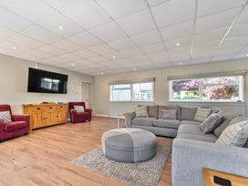 A living room with gray sectional sofa and round ottoman on rug two red armchairs wooden cabinet with wall mounted TV at Bedingfield House nr Debenham Debenham