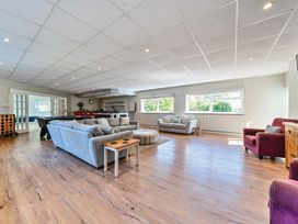 A large living room with grey sofas, a red armchair, a round ottoman, wooden flooring, and a bar area at Bedingfield House, nr Debenham in Debenham