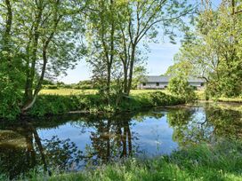 A pond with trees and grass surrounding it and a building in the background at Bedingfield House nr Debenham Debenham
